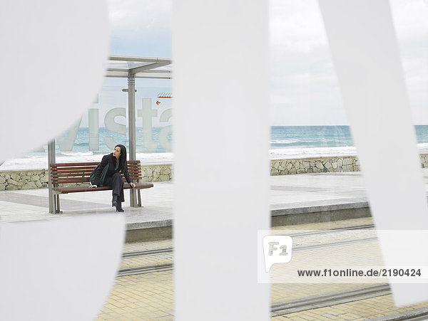 Frau  die an der Straßenbahnhaltestelle wartet  durch einen großen Schriftzug auf dem Glasdach gesehen. Alicante  Spanien.