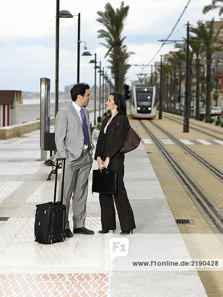 Geschäftsmann und Geschäftsfrau im Gespräch auf dem Bürgersteig mit der Straßenbahn