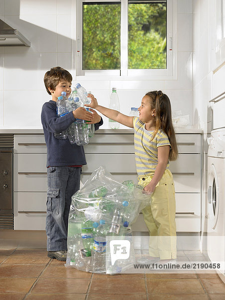 Junge (6-8) und Mädchen (4-6) teilen sich Recycling-Aufgaben in der Küche.