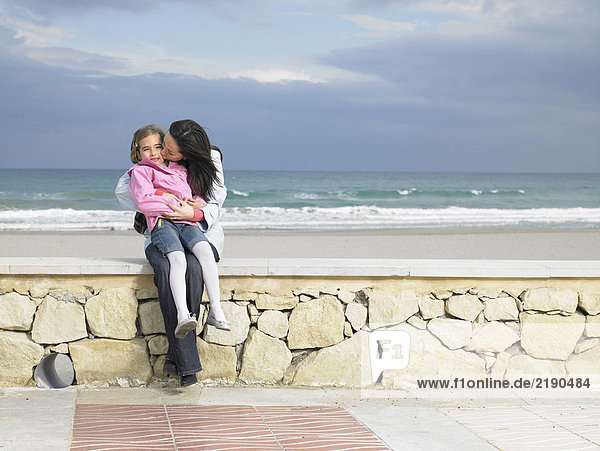 Mutter und Tochter (6-8) an der Wand am Strand sitzend