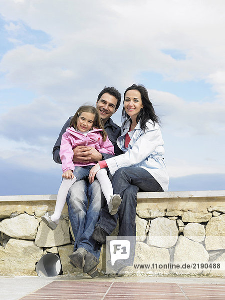 Parents and daughter (6-8) sitting on wall  smiling  portrait