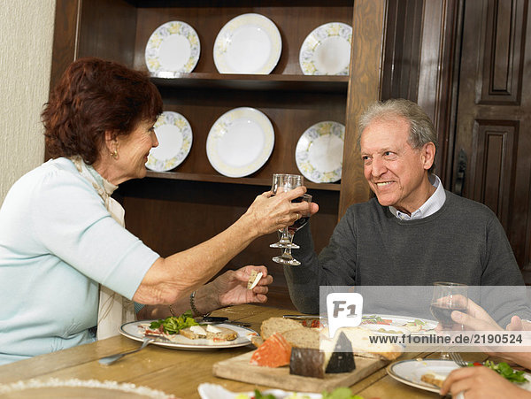 Seniorenpaare stoßen sich beim Familienessen mit Wein an.
