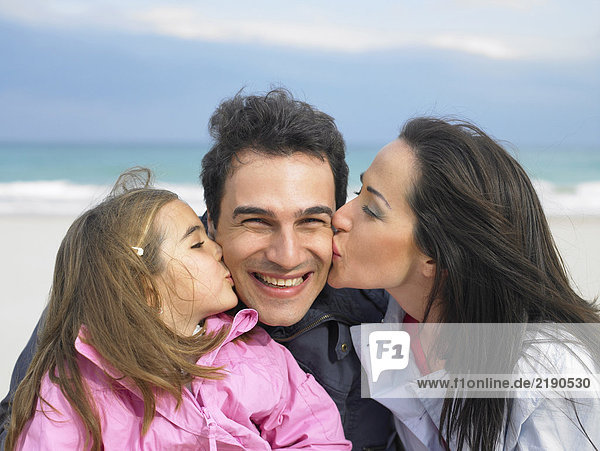 Mutter und Tochter (6-8) küssen den Vater von beiden Seiten am Strand. Alicante  Spanien.