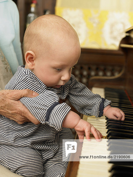 Senior Großmutter hält Baby Enkel (1-3 Monate) drücken Piano-Tasten