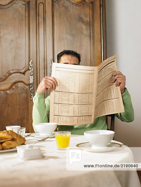 Mann sitzt am Frühstückstisch und liest Zeitung