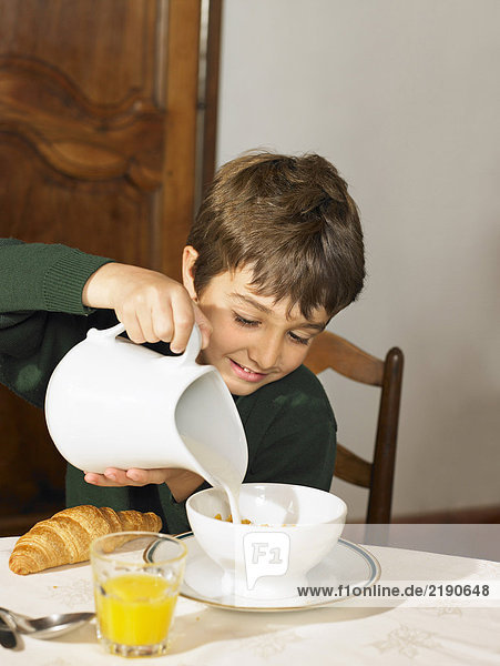 Junge (6-8) beim Frühstück Milch über Müsli gießen