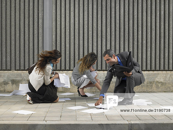 Two businesswomen and one businessman trying to recover papers blowing about pavement  Alicante  Spain