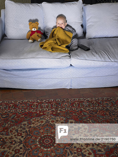 Baby (1-3 Monate) beim Fernsehen auf dem Sofa mit Teddybär. Alicante  Spanien.