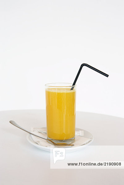 Ein Glas Orangensaft mit Strohhalm.