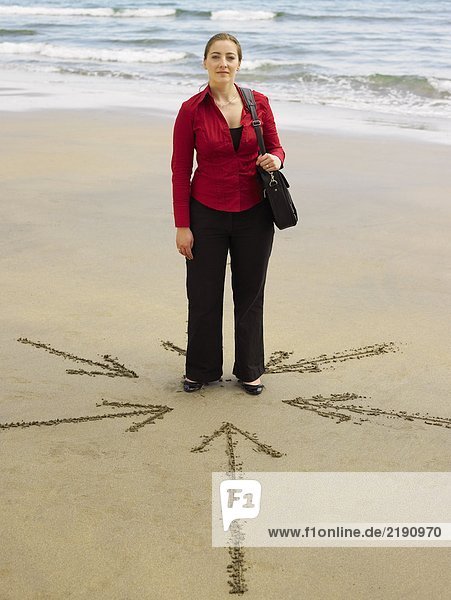 Frau am Strand mit Pfeilen im Sand um sie herum.