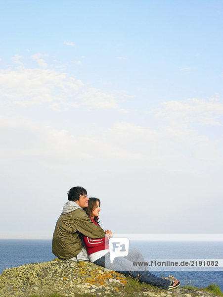 Ein Paar sitzt auf einer Klippe mit Blick aufs Meer.