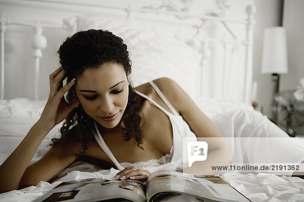 Woman reading magazine on bed.