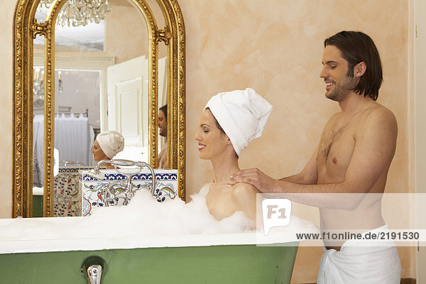Young man smiling massaging back of woman smiling in bath  side view