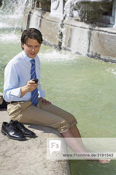 Businessman in fountain on cell phone.