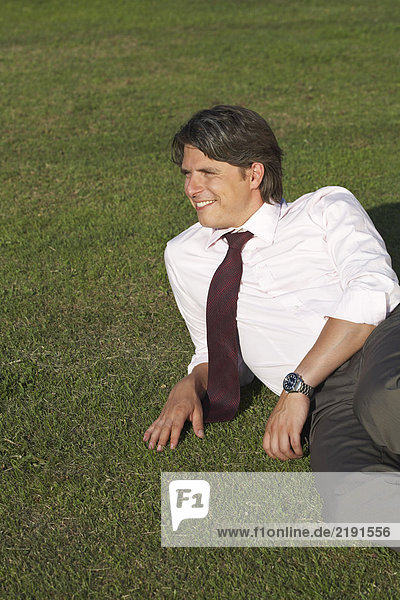 Businessman sitting in meadow laughing.
