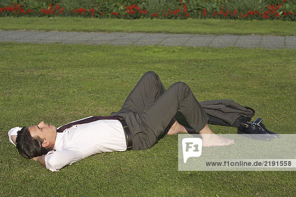 Businessman lying in meadow bare feet shoes and jacket nearby view from side.