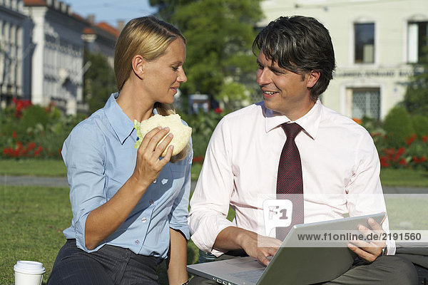 Businessman and businesswoman sitting in park working.