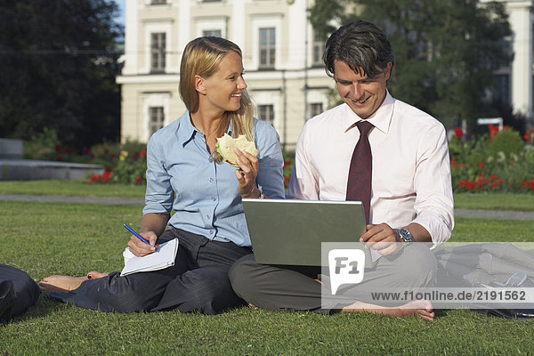 Businessman and businesswoman sitting in park working.