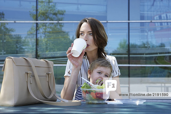 Geschäftsfrau und ihr Kind beim gemeinsamen Mittagessen im Freien.