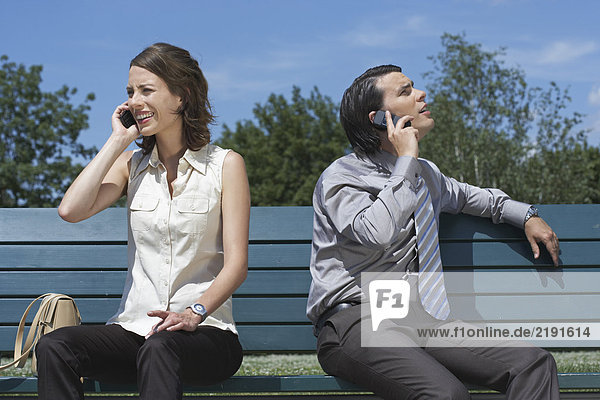 Geschäftsmann und Frauen sprechen auf dem Handy  während sie draußen auf der Bank sitzen.