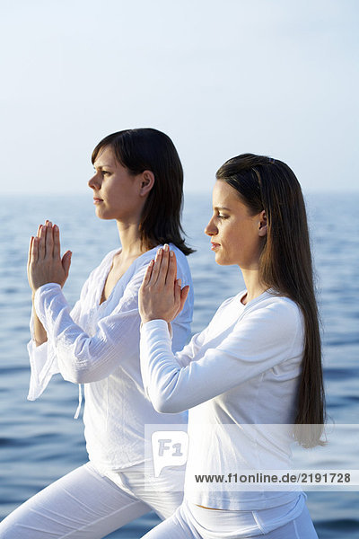 Two young women doing yoga by the sea.