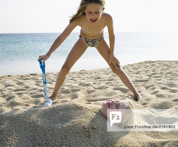 Young girl burying young boy in the sand at the beach .