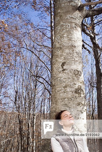 Frau  die sich an einen Baum lehnt und lächelt.