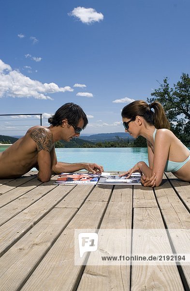 Paar Sonnenbaden am Schwimmbad mit Zeitschriften