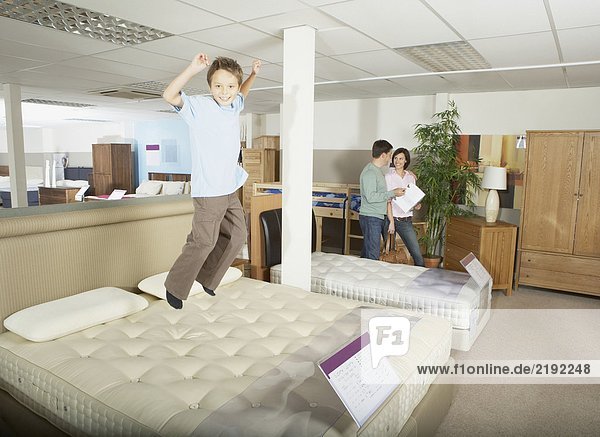 Boy jumping on bed in furniture store.