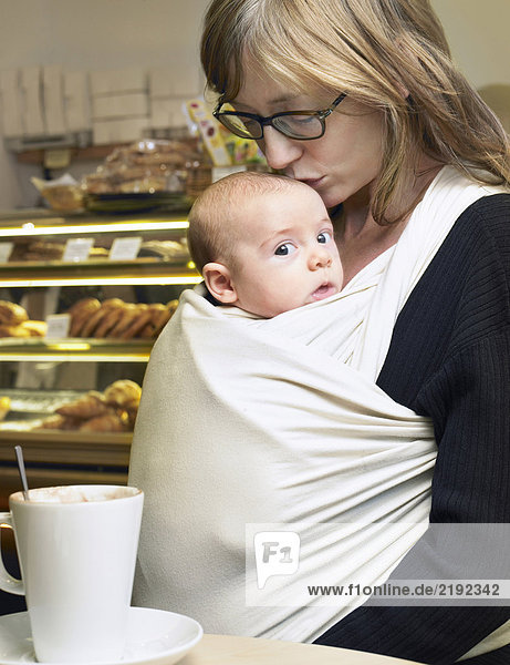 Mutter küsst Babysohn (1-3 Monate) auf dem Kopf im Cafe