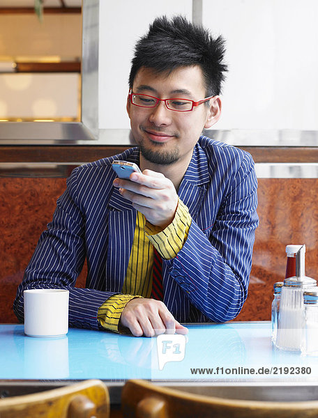 Junger Mann sitzt im Cafe mit dem Handy und lächelt