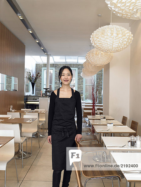 Junge Kellnerin steht im leeren Restaurant  lächelnd  Portrait