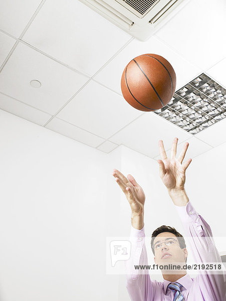 Geschäftsmann in einem Büro  der einen Basketball wirft.
