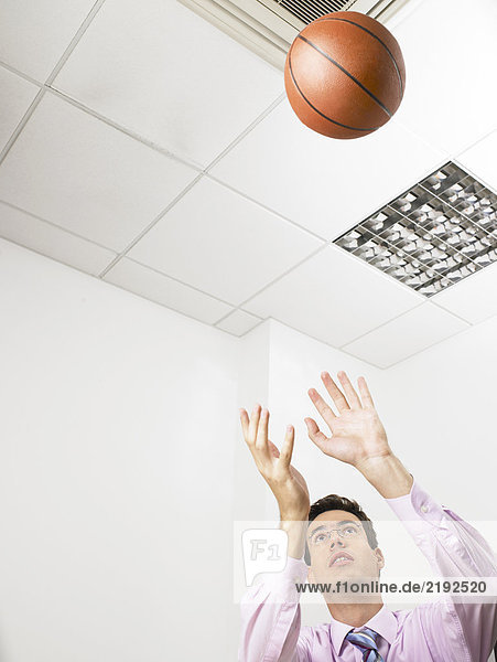 Geschäftsmann in einem Büro  der einen Basketball wirft.
