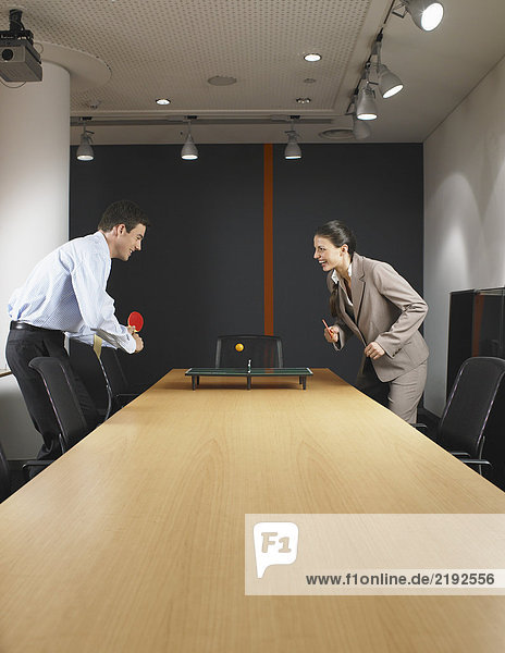 Mann und Frau spielen Miniatur-Pingpong am Konferenztisch