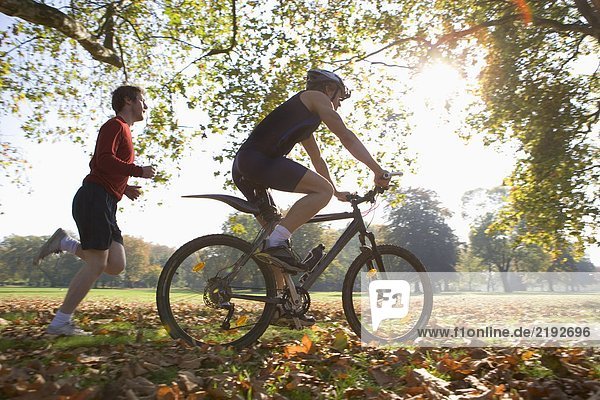Cyclist riding mountain bike with jogger following.