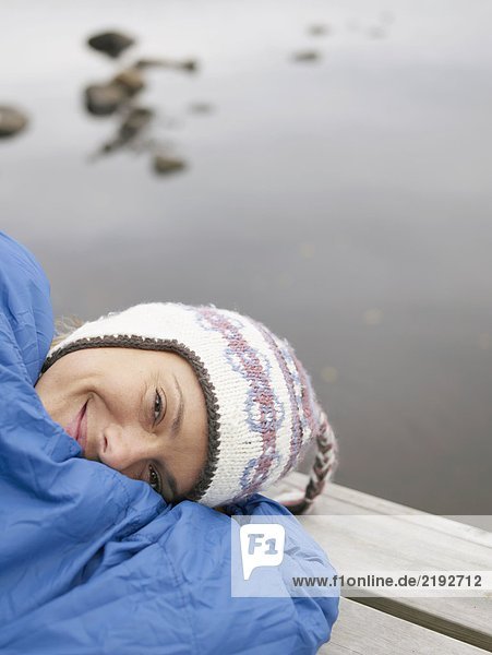 Frau mit auf einem Dock im Schlafsack lächelnd.