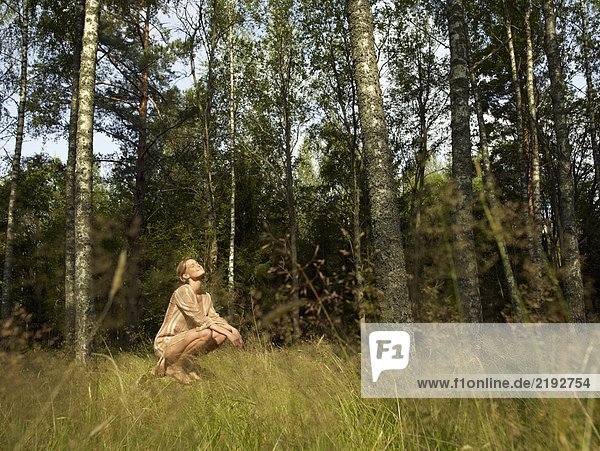 Frau kauert auf einem großen Felsen im Wald und lächelt.