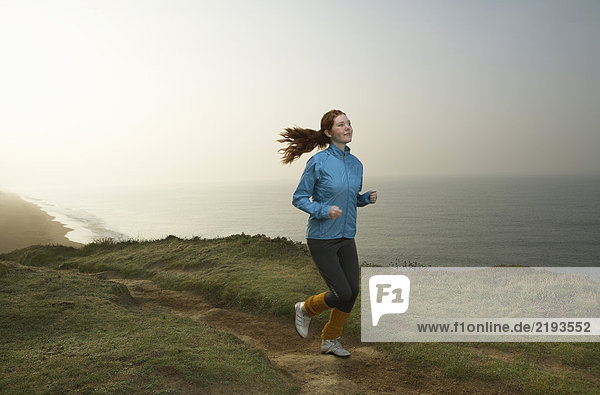A young Woman jogging along a cliff path.