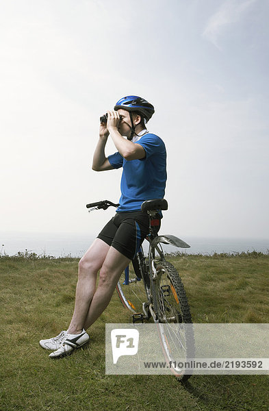 Ein männlicher Radfahrer schaut durch ein Fernglas.
