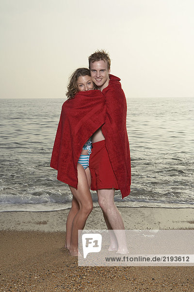 Paar in Handtuch gewickelt am Strand.