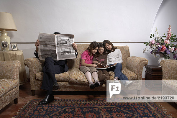 Mann liest Zeitung auf Sofa mit Töchtern(5-11)