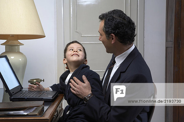 Son (4-6) smiling at father while using laptop