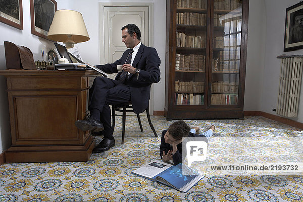 Vater sitzend mit Blick auf Laptop und Sohn (4-6) Lesebuch