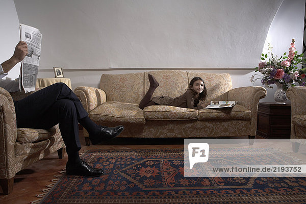Mann liest Zeitung mit Tochter (5-7) Lesebuch auf Sofa