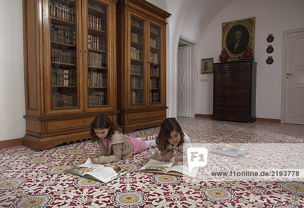 Girls (6-11) lying on floor reading books