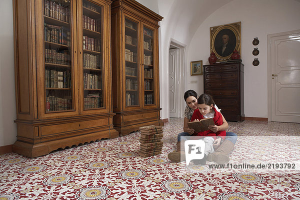 Mutter und Tochter (5-7) sitzen auf dem Boden und lesen Bücher.