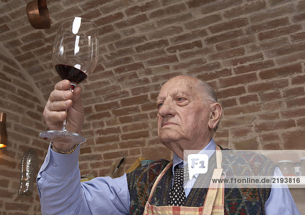 Älterer Mann beim Betrachten von Wein im Glas