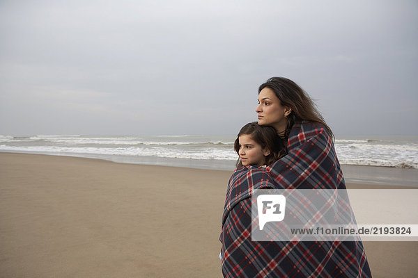 Mother and daughter (9-11) wrapped in blanket on beach