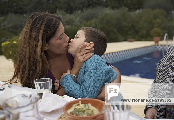 Mutter küssend Sohn (4-6) am Tisch  draußen